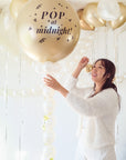 Woman holding a balloon with 'Pop at midnight!' text in a decorated room.