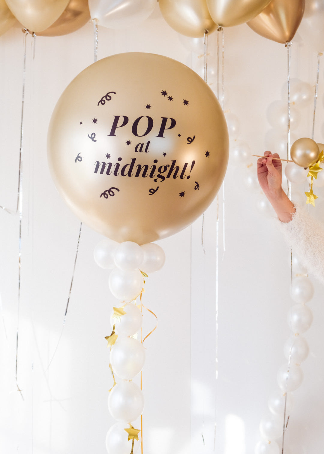Gold balloon with 'Pop at midnight!' text in a festive setting with white and gold balloons.