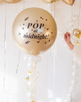 Gold balloon with 'Pop at midnight!' text in a festive setting with white and gold balloons.