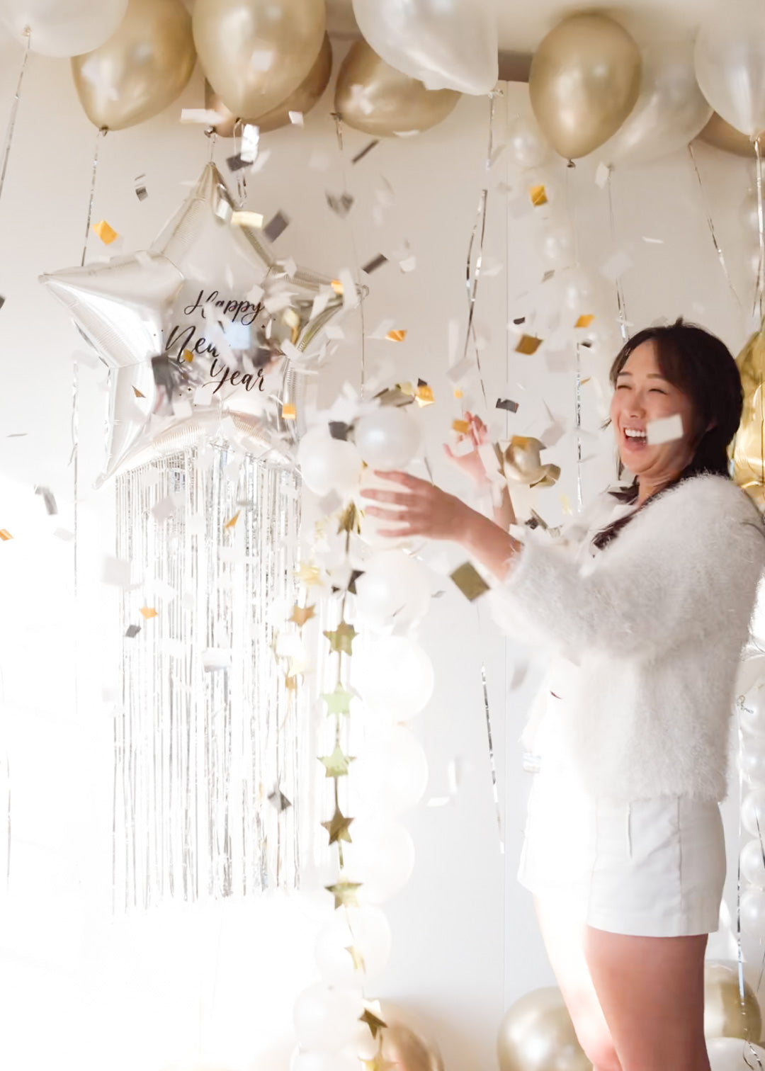 Woman in a white dress celebrating with balloons and confetti in a festive setting.