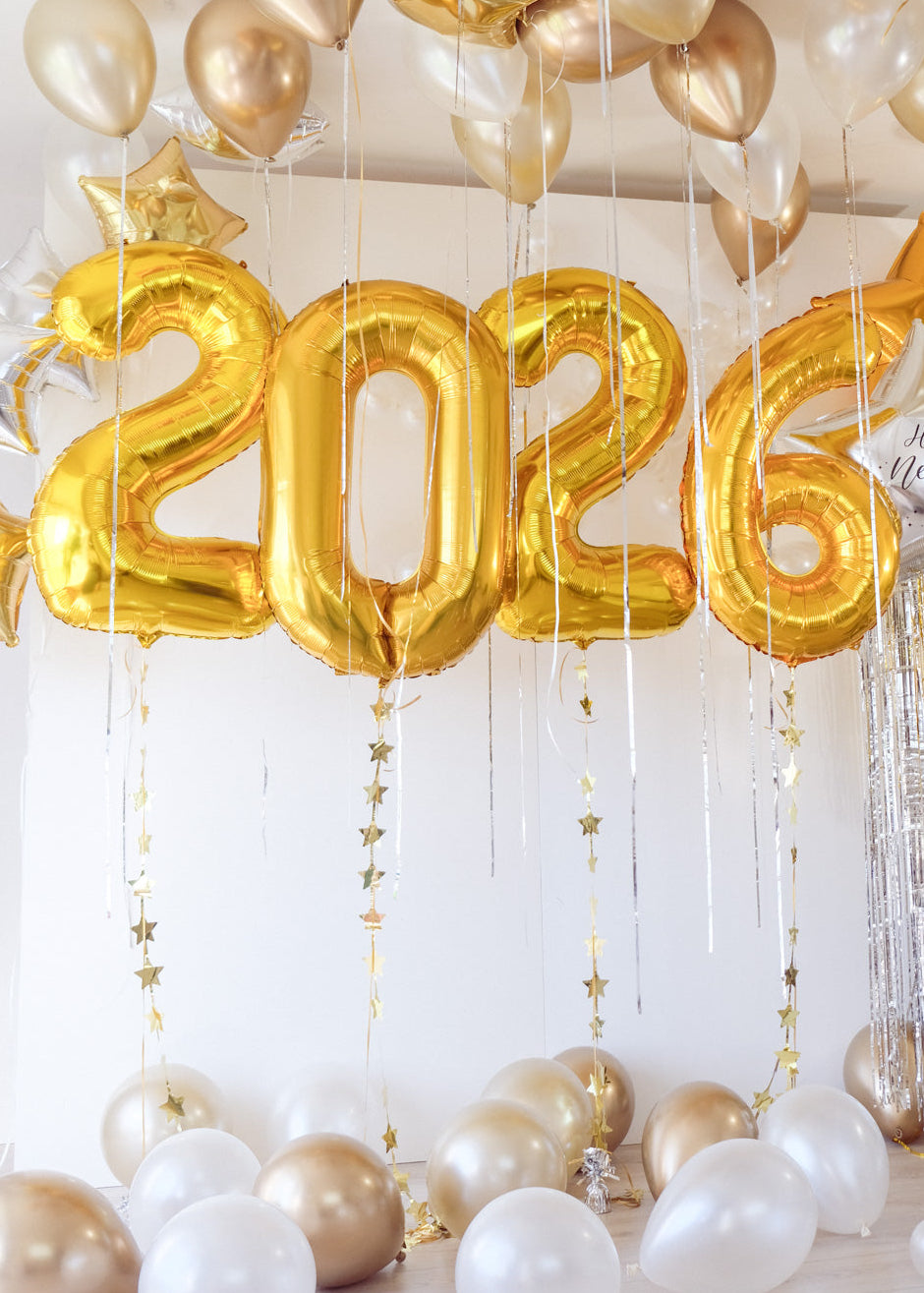 NYE BALLOONS 2026 in gold with gold and white balloons floating above in the ceiling and on the floor.