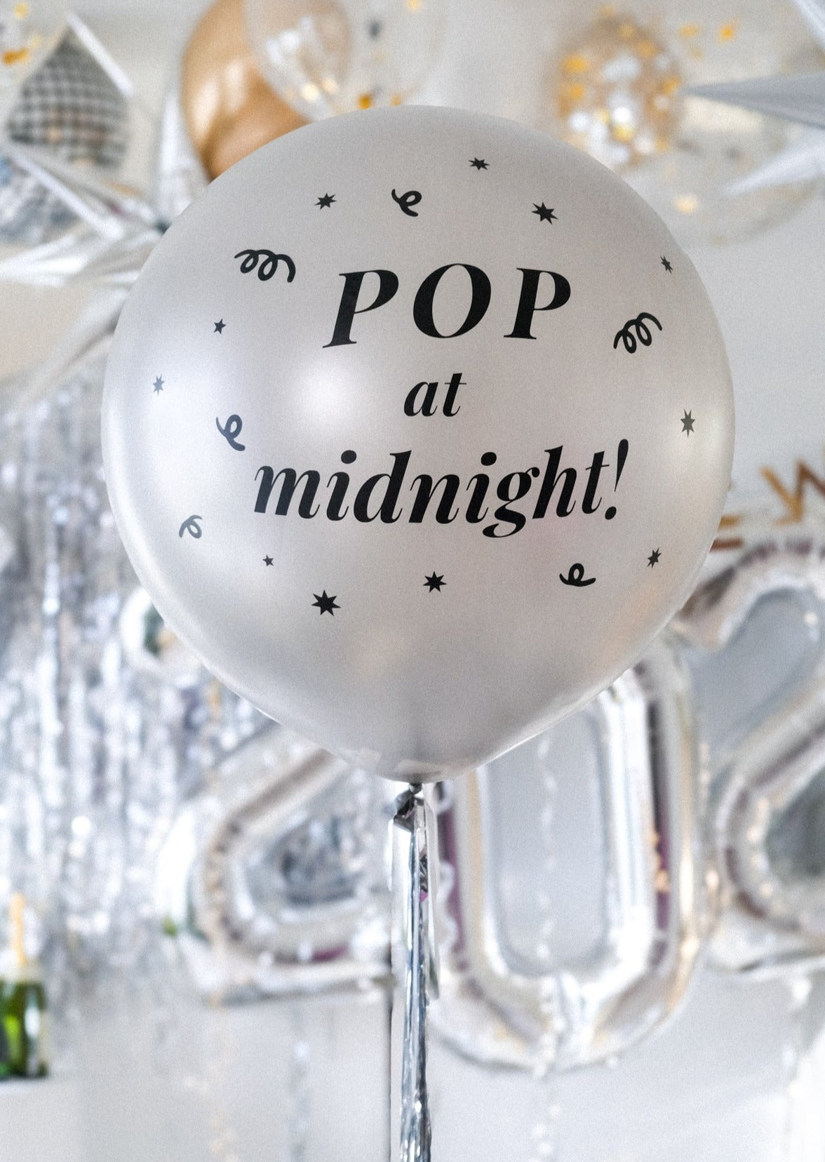 A silver round balloon filled with text "Pop at Midnight" in front of festive background