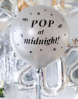 A silver round balloon filled with text "Pop at Midnight" in front of festive background