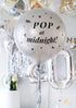 A silver round balloon filled with text "Pop at Midnight" in front of festive background