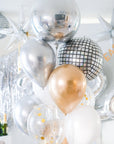A selection of balloons featuring metallic finishes including a silver mirror orb, with confetti and gold-colored balloons, set against a festive background.