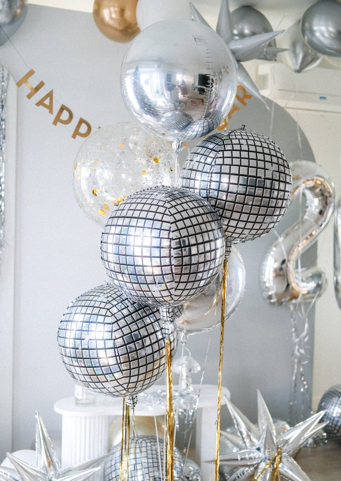 a set of round metallic balloons in silver, disco and confetti in front of a decorated backdrop