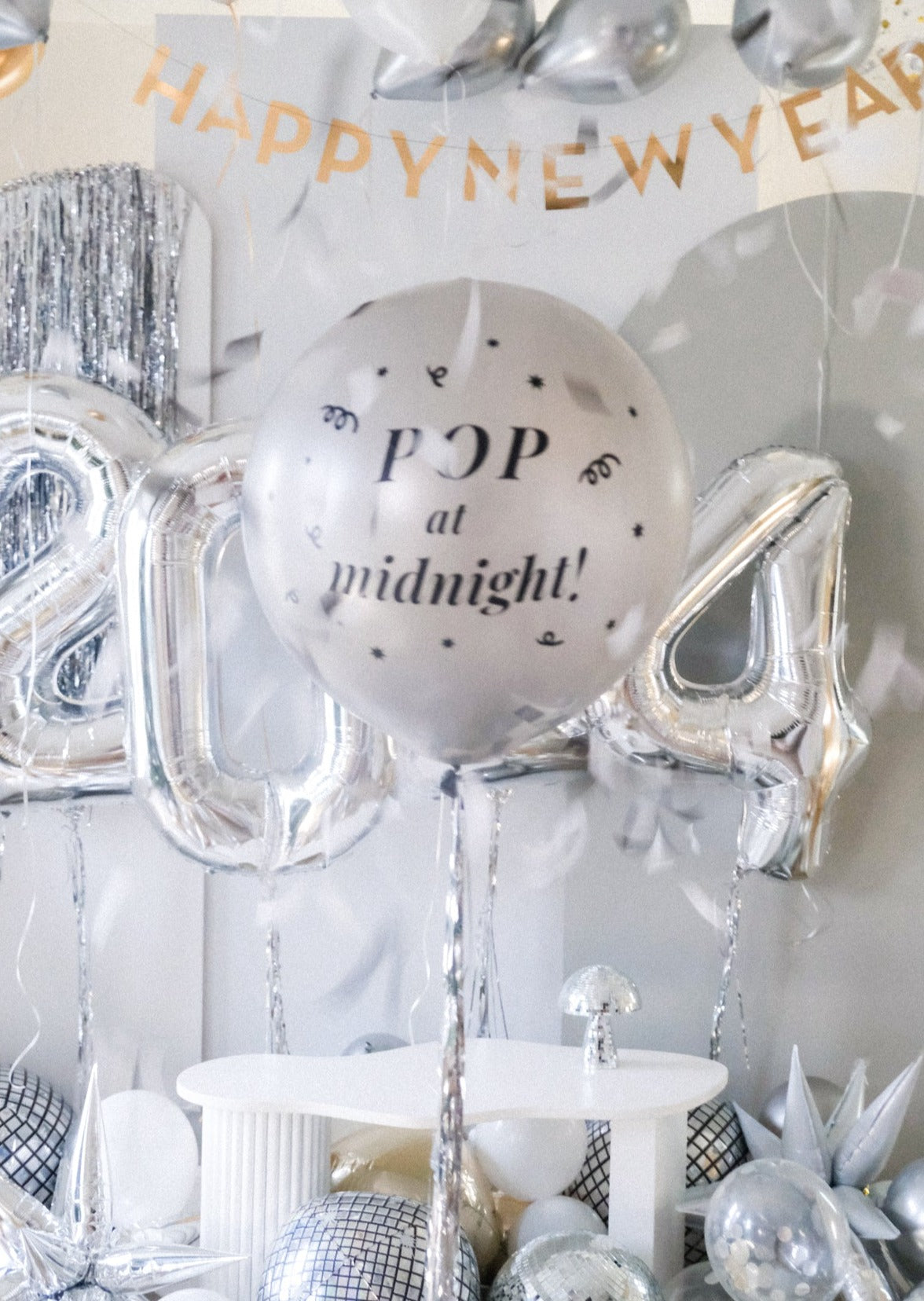 A silver round balloon filled with text "Pop at Midnight" in front of festive background