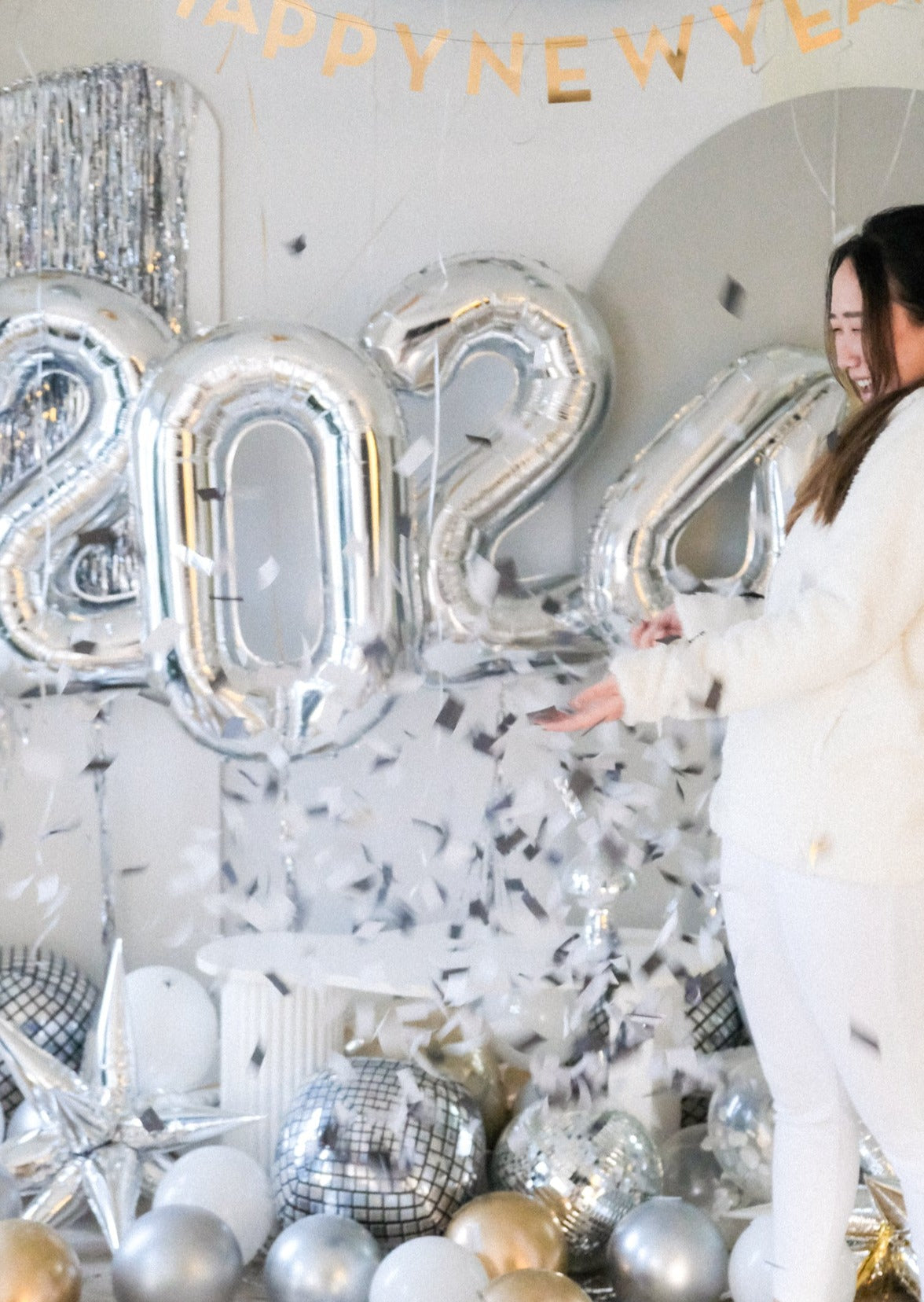 A girl wearing white with confetti flying everywhere from the popped balloon