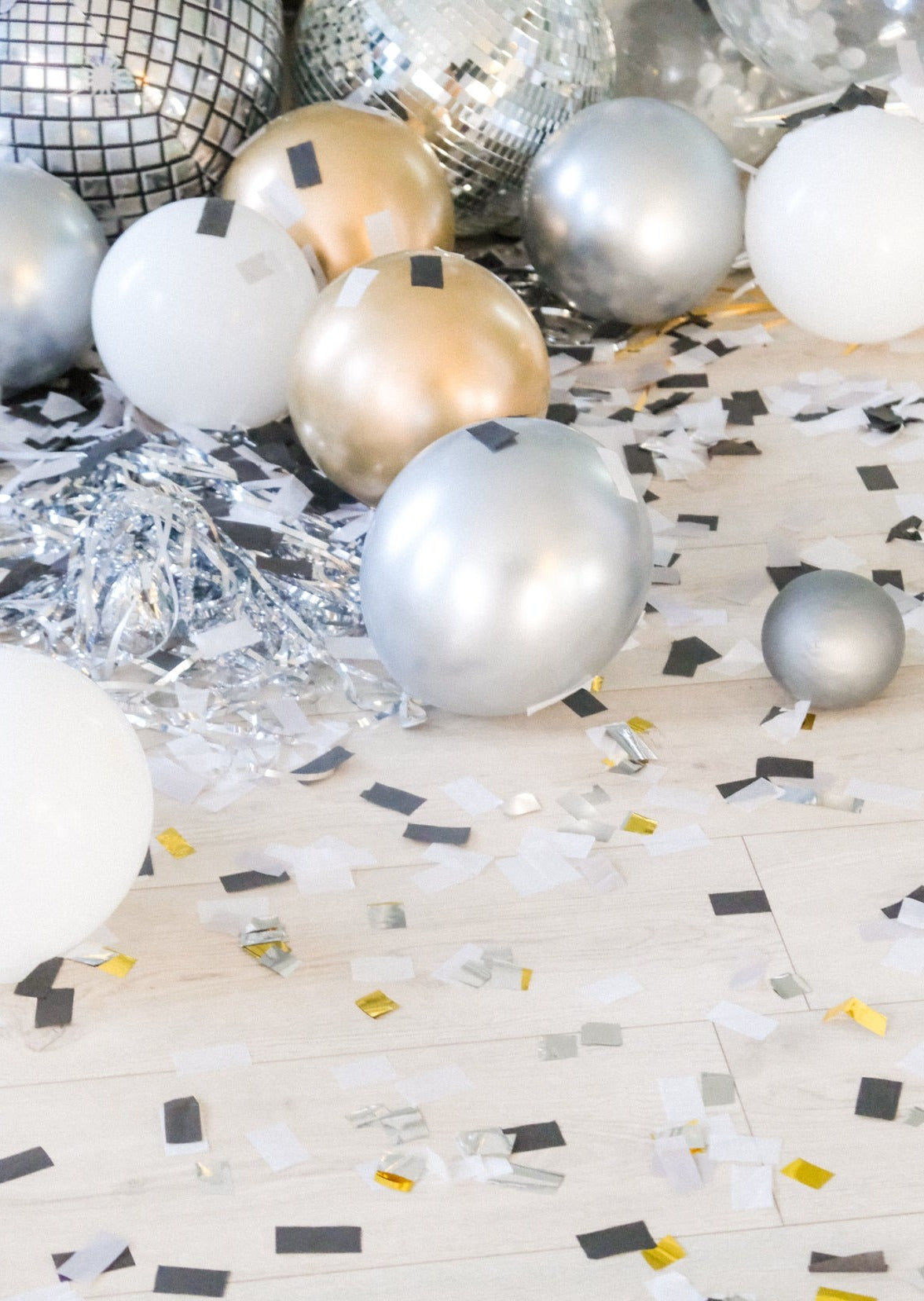Confetti and balloon filled floor with some silver metallic tinsel and portions of disco balloon and ball