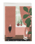 A greeting card featuring an illustration of a cat looking out of a window, with a plant and a cactus inside. The window has pink curtains, and there is a sense of intimacy in the composition.
