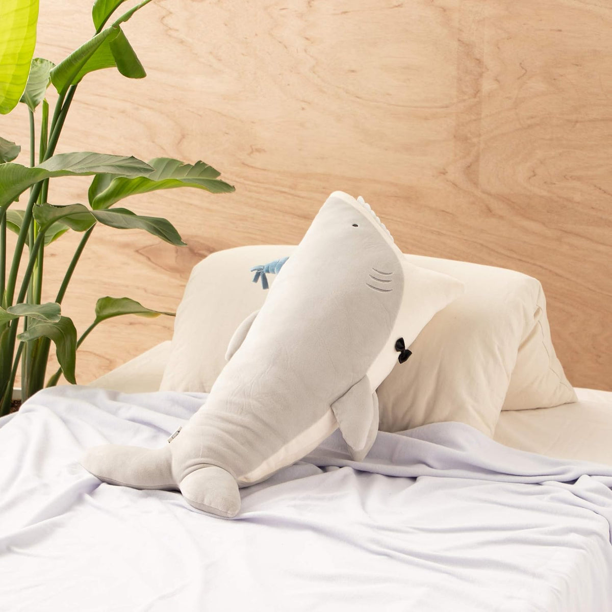 stuffed animal of grey shark wearing a blue party hat, in bedroom setting background