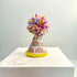 A colorful party hat for pets with pastel rainbows and a pom pom on top, displayed on a white surface.