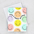 A pastel smiley birthday card with a design of smiley faces in various colors on a white background, and the text 'HAVE A HAPPY BIRTHDAY' in the center. The card is displayed with a matching envelope.