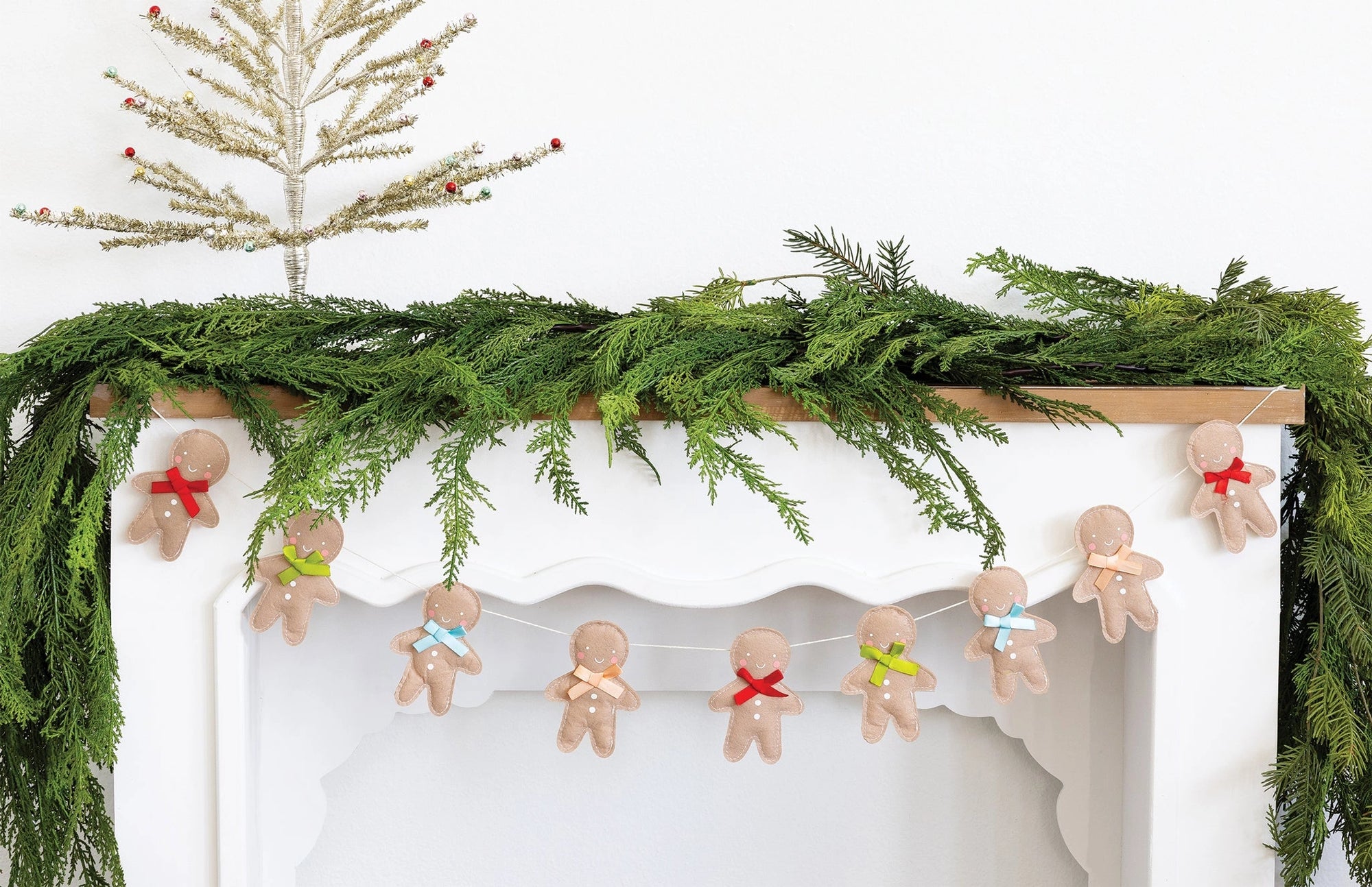 Decorative Christmas mantel with greenery, gingerbread men garland, and a small tree.