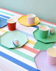 Table setting with a rainbow striped table cover and rainbow paper plates and cups