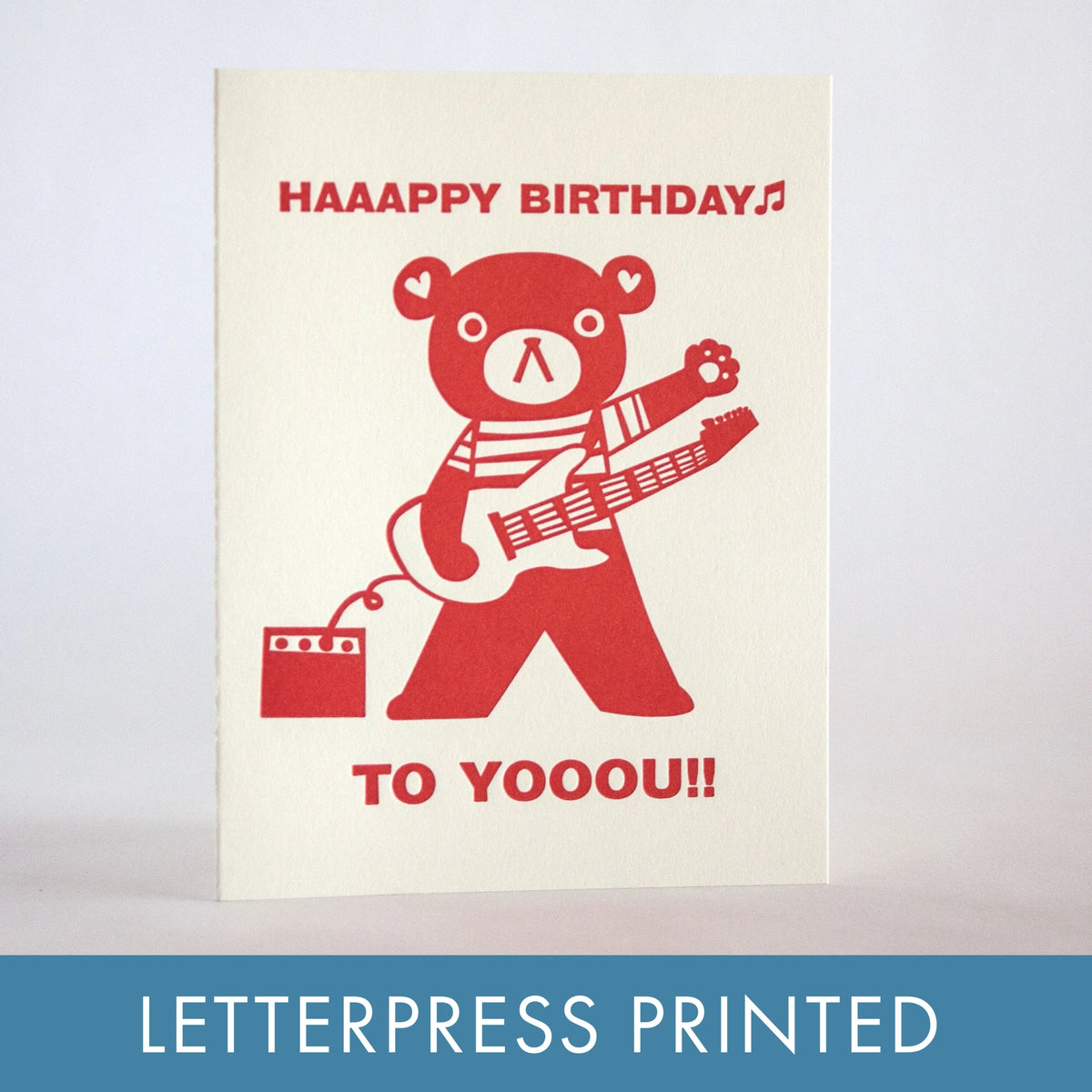 Letterpress printed birthday card with red bear playing guitar on a beige background
