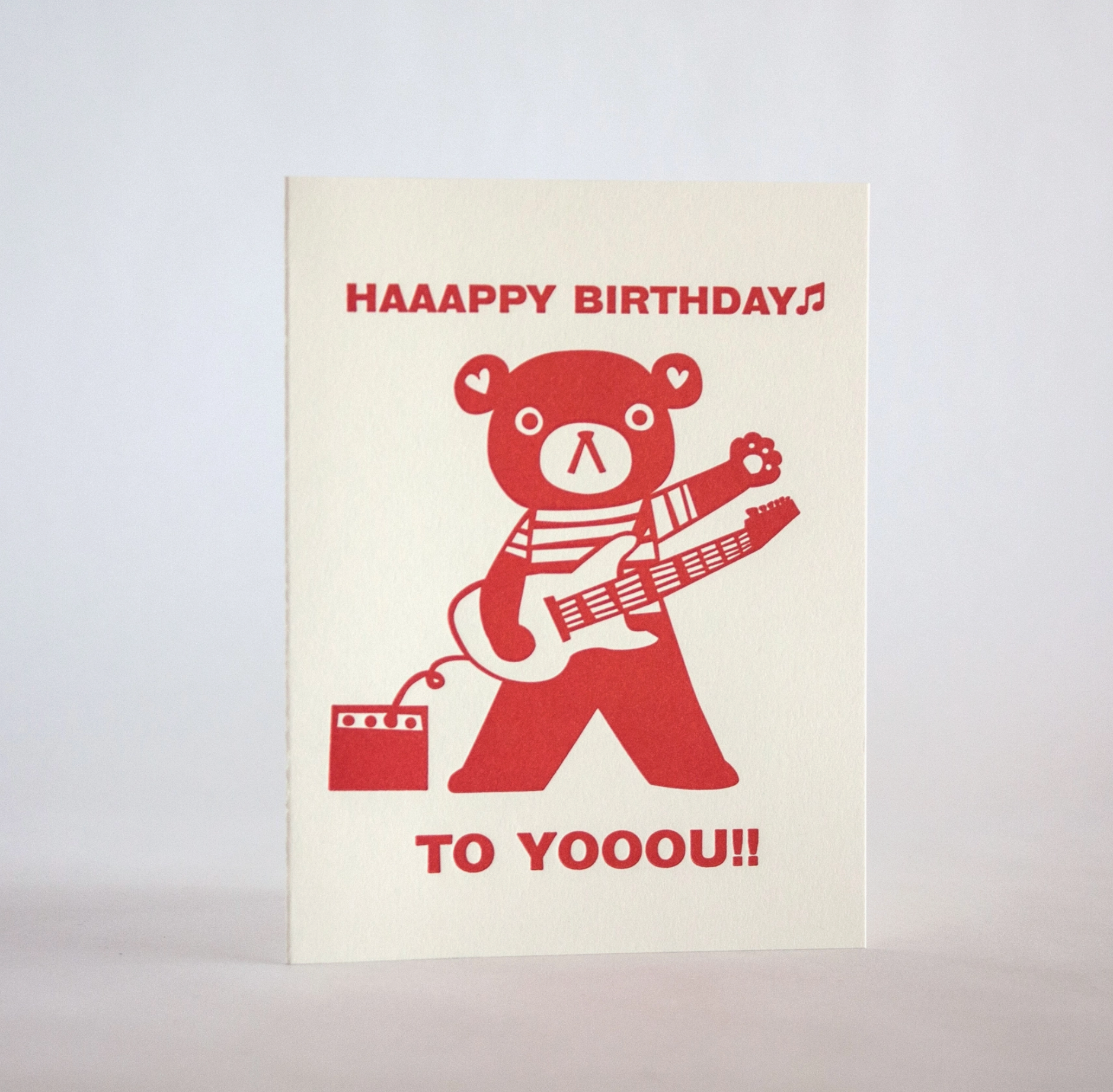 A greeting card with a cartoon bear wearing a striped shirt and playing a guitar, with the text 'HAPPY BIRTHDAY' and 'To YOUUU!!'.