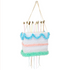 A decorative birthday cake piñata with peach pink, blue and mint tissue paper festooning, and striped paper straw 'candles' topped with gold foil 'flames'.