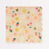 A folded paper napkin with a colorful design featuring smiley faces, mushrooms, a rainbow, fruit, stars, hearts, and flower power, adorned with shiny gold foil details.