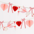 A romantic Parisian garland featuring pink and red paper lovebird pennants, gingham ribbon bows, and 3D honeycomb hearts with paper notes in beaks, displayed against a white background.