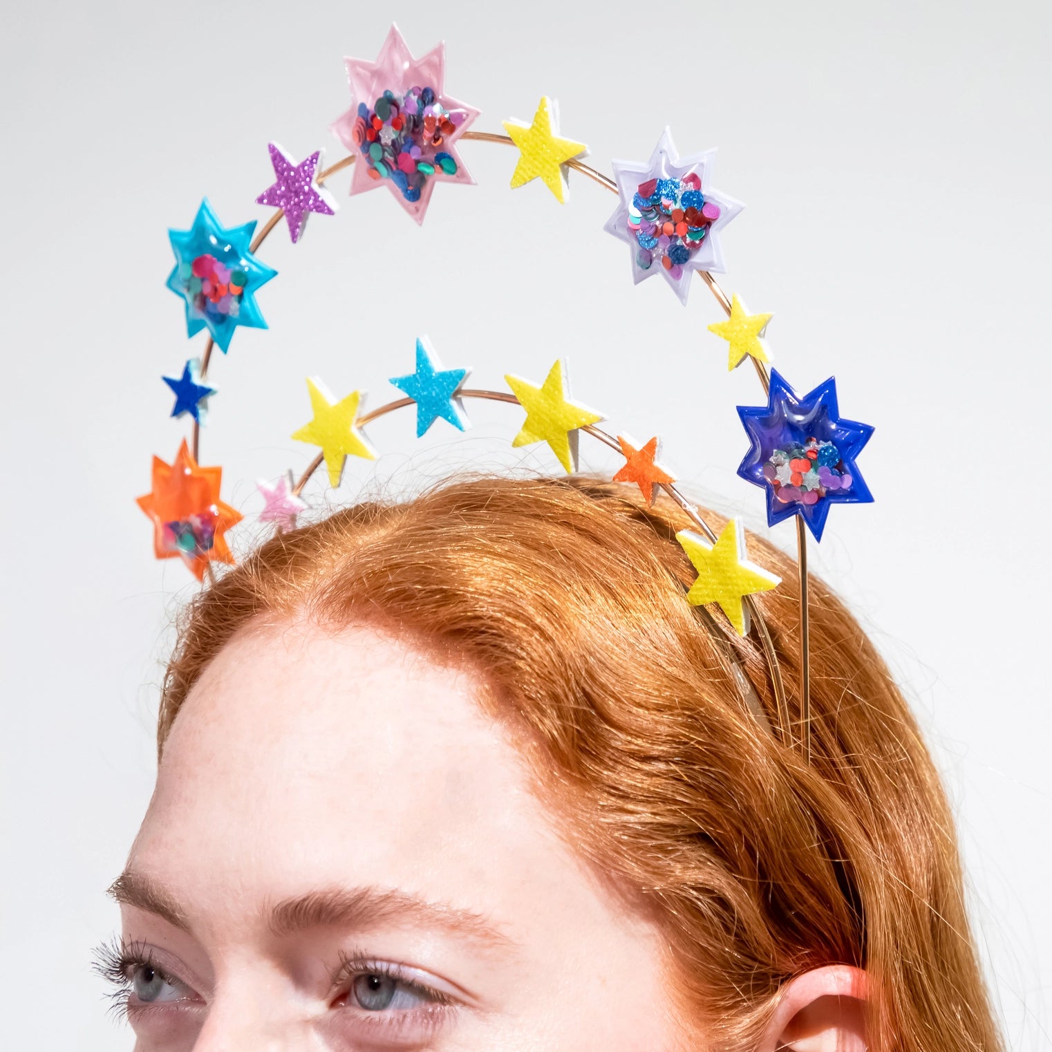Colorful star-shaped headband worn by a person with red hair on a light gray background