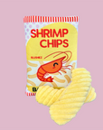 A canvas dog toy shaped and designed like a bag of shrimp chips, with a red crab graphic and the product name 'Shrimp Chips' printed on it. The toy is in a yellow color, and there is a squeaker in the center.
