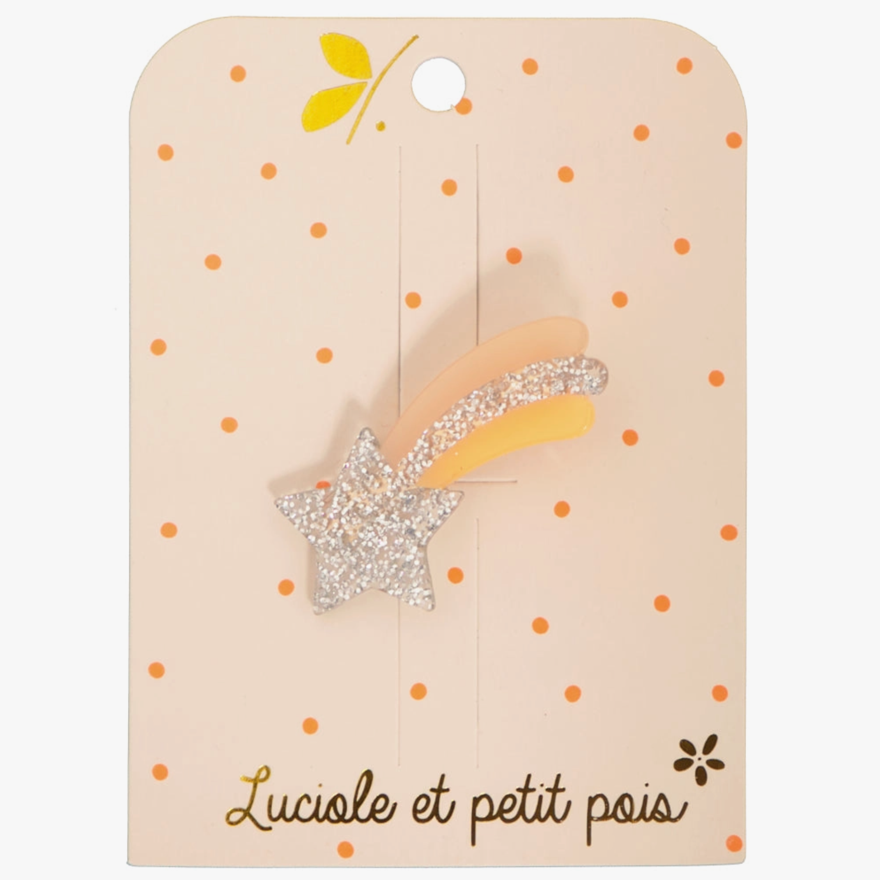 A silver and orange glittery hair clip in the shape of a shooting star, attached to a beige card with polka dots and a small flower illustration.