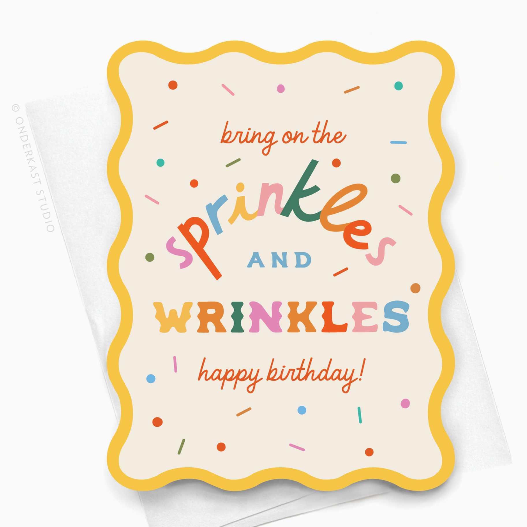 A birthday card with a colorful design, featuring the text 'SPRINKLES AND WRINKLES HAPPY BIRTHDAY!' surrounded by various colorful sprinkles on a light background, also showing a yellow envelope with a square flap.