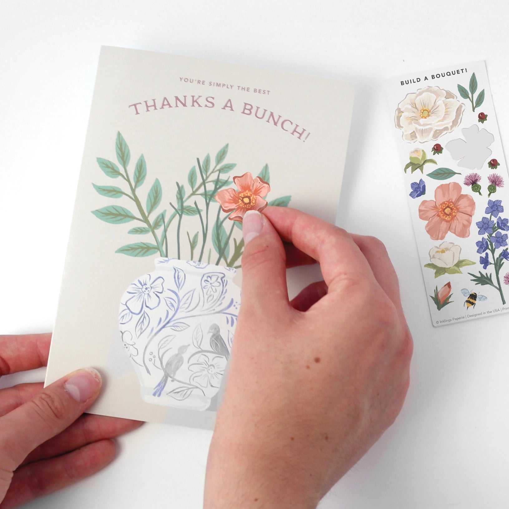 Hand holding a card with floral designs and a sticker sheet on a white background
