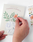 Hand holding a card with floral designs and a sticker sheet on a white background