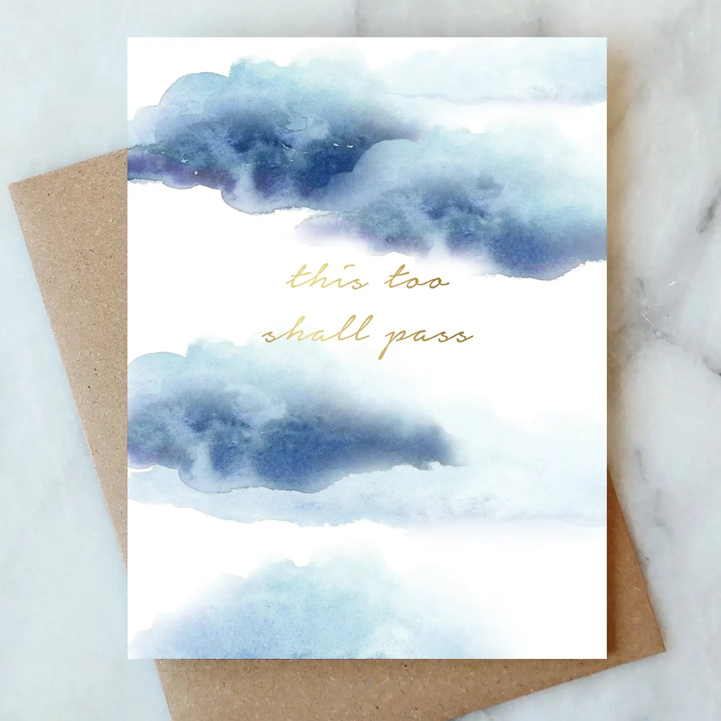 Card with watercolor clouds and 'this too shall pass' text on a marble surface