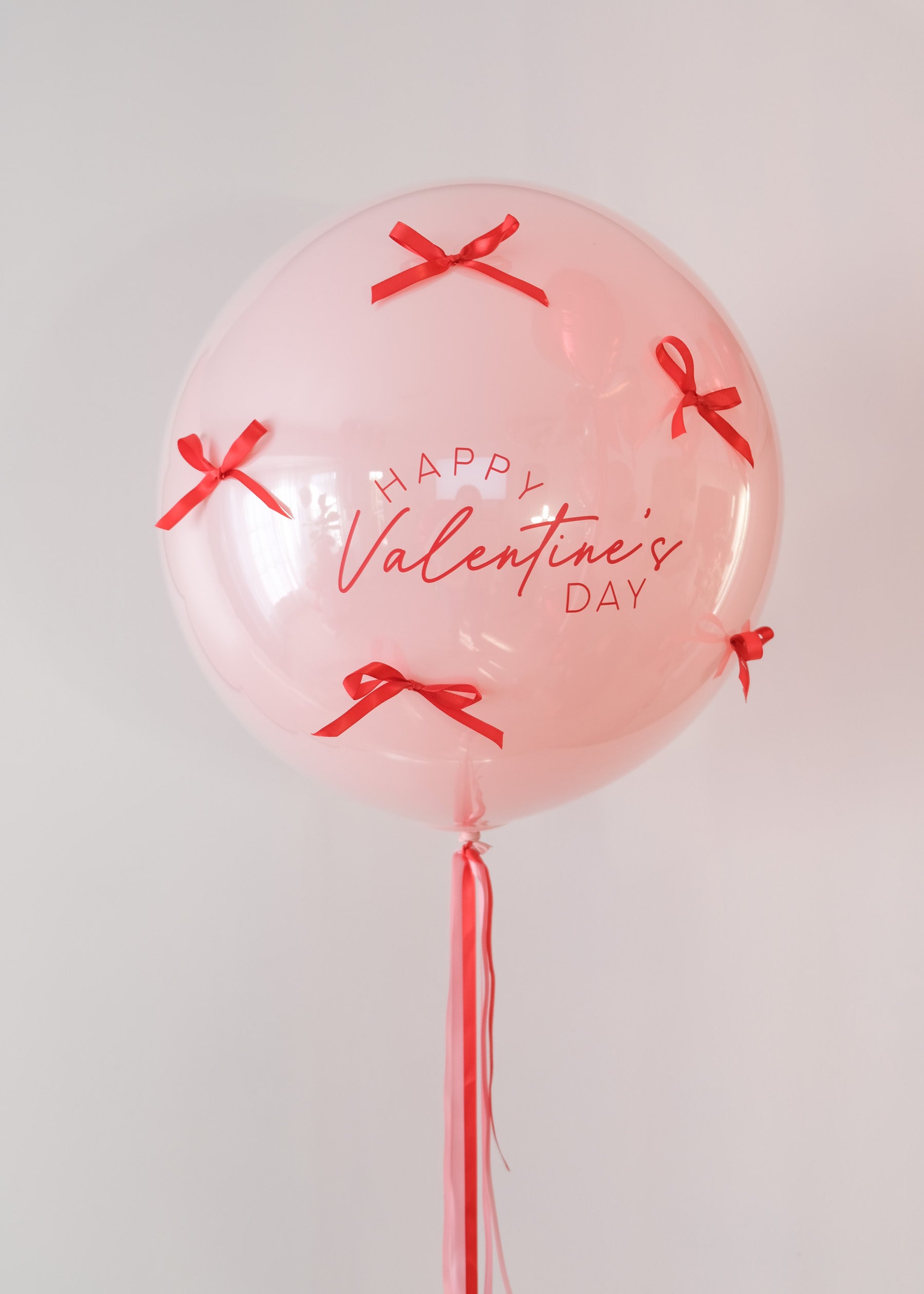 Pink balloon with 'Happy Valentine's Day' text and red ribbons on a light gray background