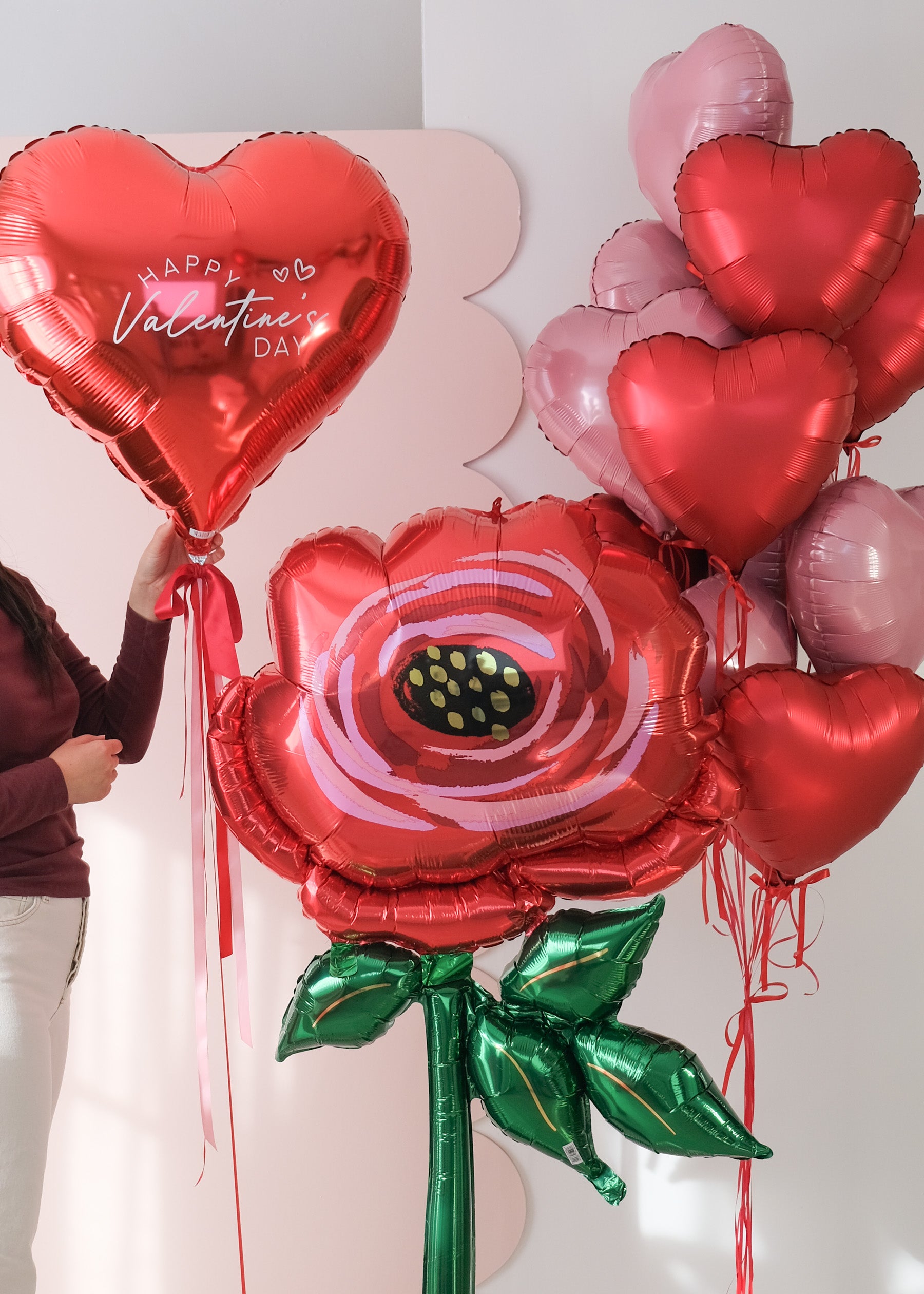 Valentine's Day-themed balloons including a heart-shaped balloon and a rose-shaped balloon with a person holding them.