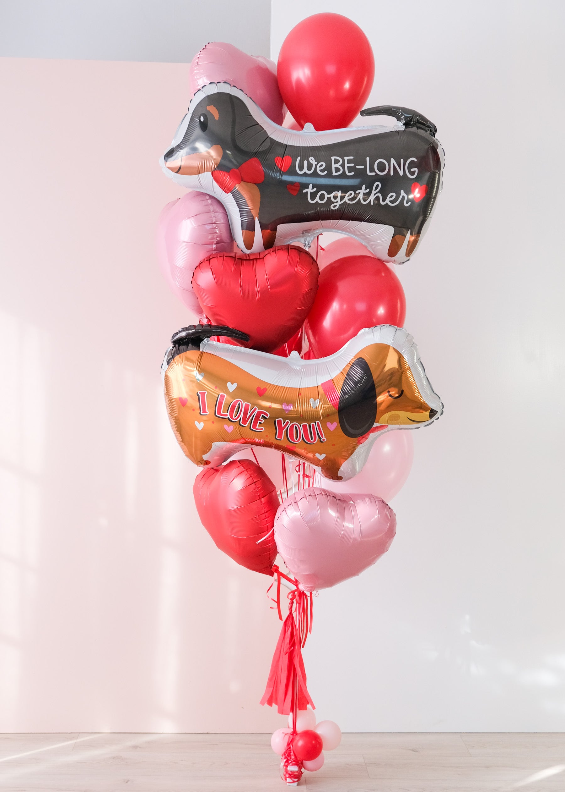 Large balloon bouquet with two dog-shaped balloons that say "We Be-Long Together" and "I Love You" with heart balloons