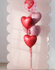 Heart-shaped balloons with a clear 'Happy Valentine's Day' balloon against a decorative pink background.
