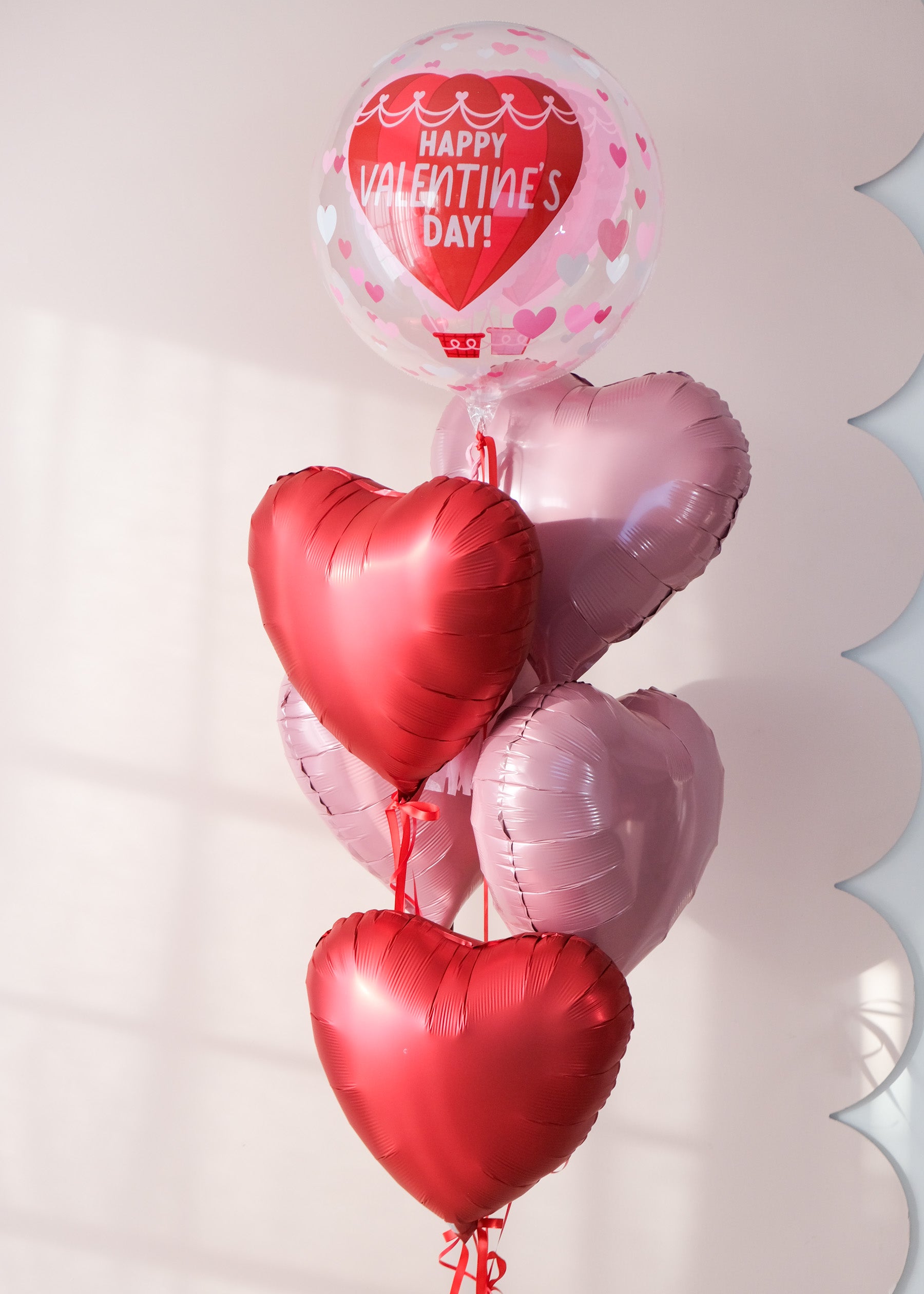 Heart-shaped balloons with 'Happy Valentine's Day!' clear ballloon, on a light pink background