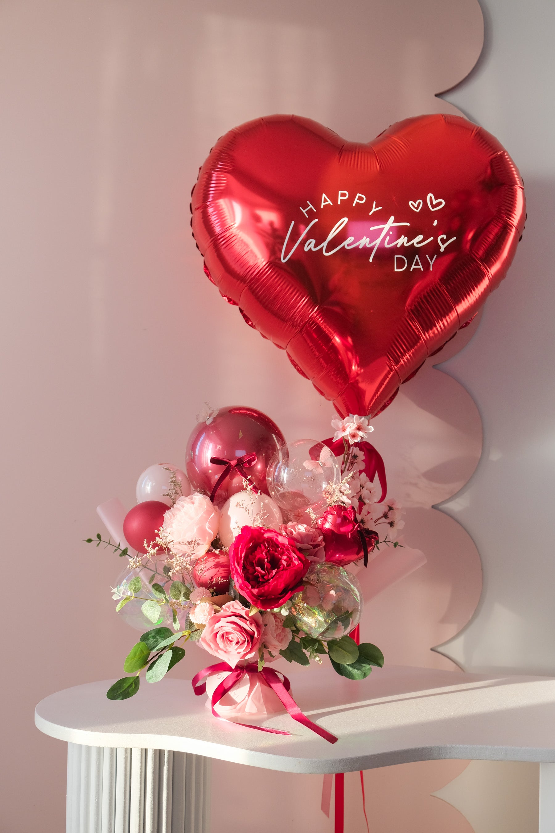 Heart-shaped 'Happy Valentine's Day' balloon with a bouquet of flowers and balloons on a white table
