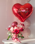 Heart-shaped 'Happy Valentine's Day' balloon with a bouquet of flowers and balloons on a white table