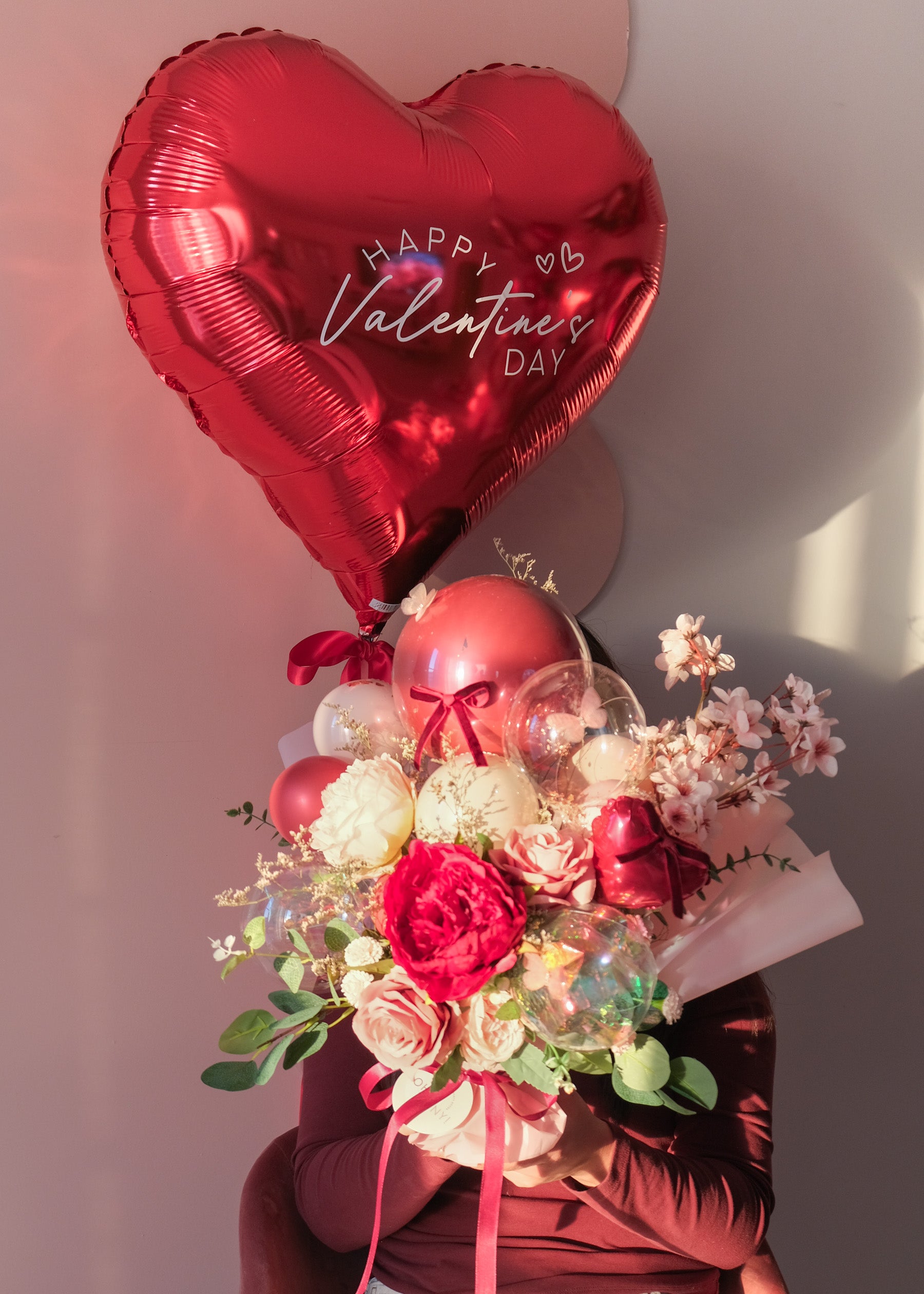a person holding a bouquet of flowers and balloons with a large red heart balloon