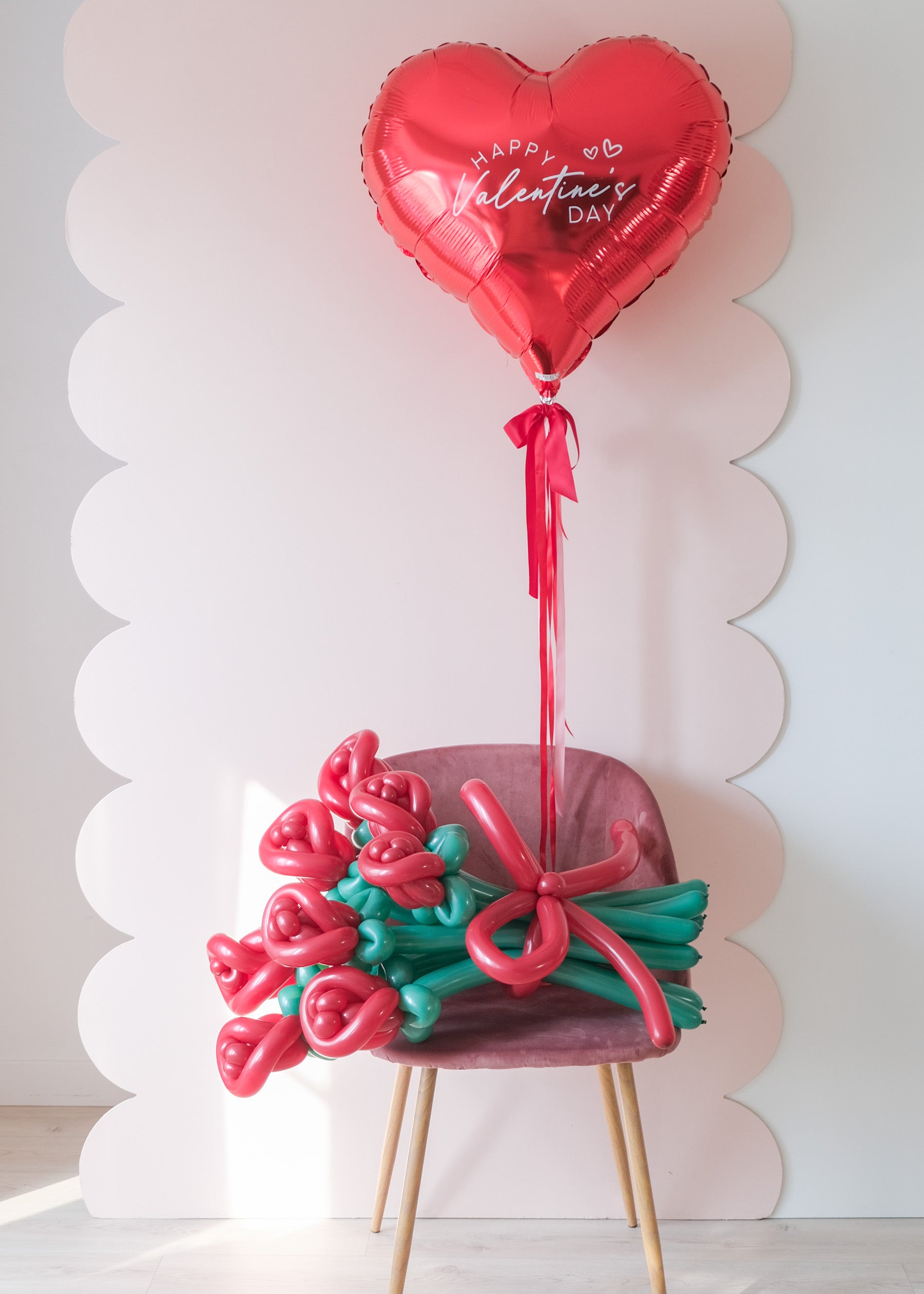 8-stem twisted rose balloon bouquet on a chair with red heart balloon 
