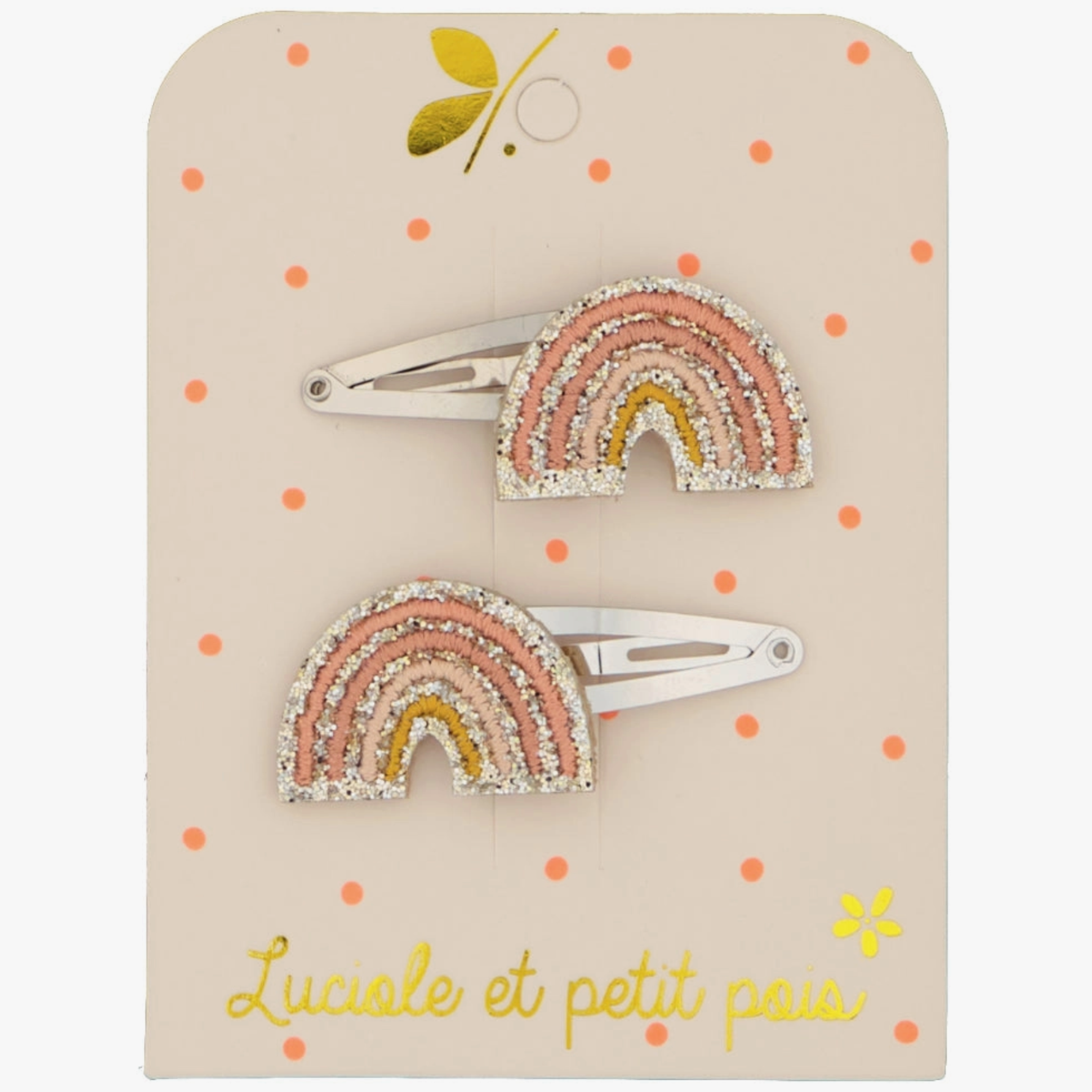 A pair of hair clips with a rainbow glitter design on a beige background, packaged on a card with polka dots.