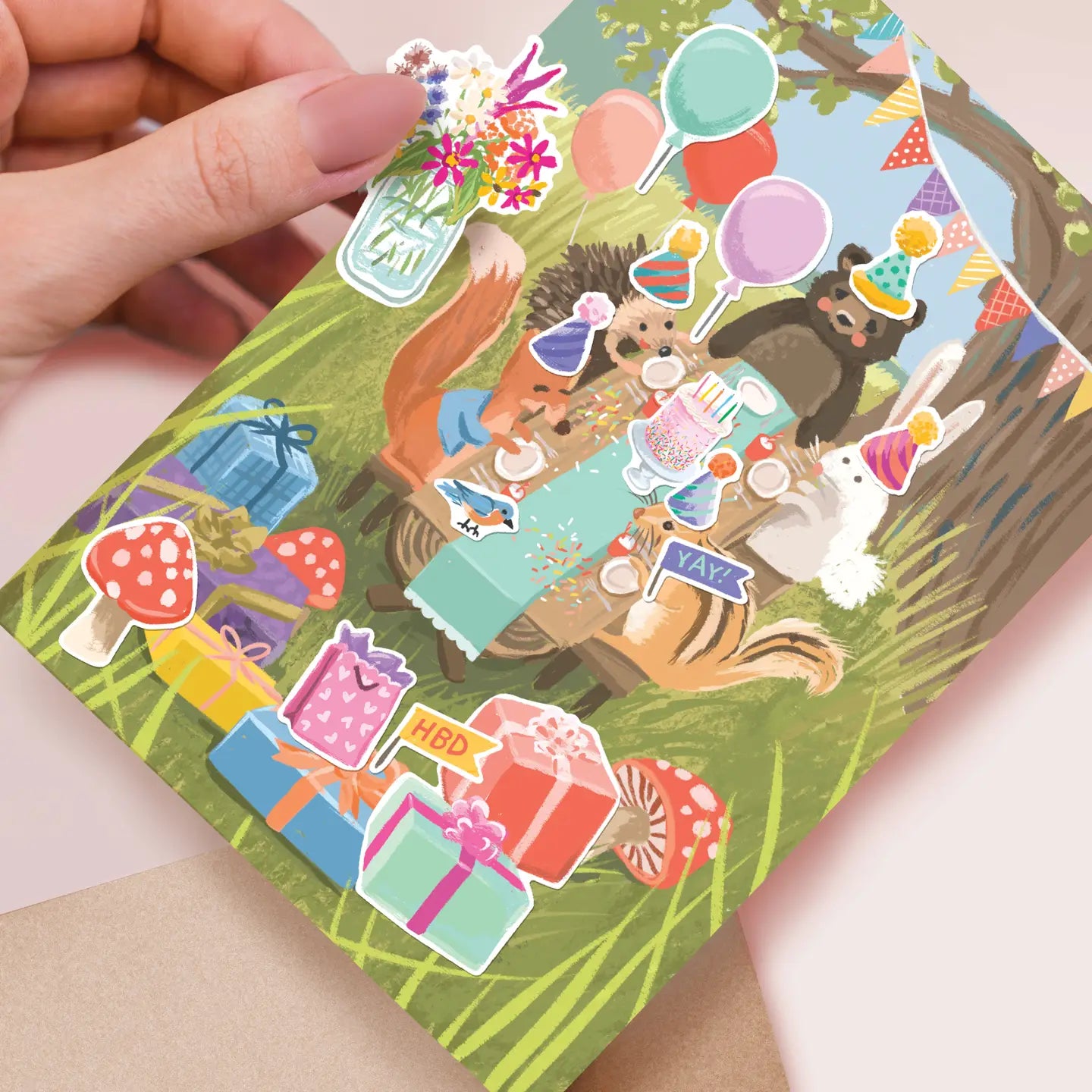Hand holding a card with colorful animal stickers on a light pink background