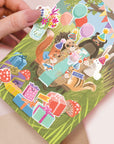 Hand holding a card with colorful animal stickers on a light pink background
