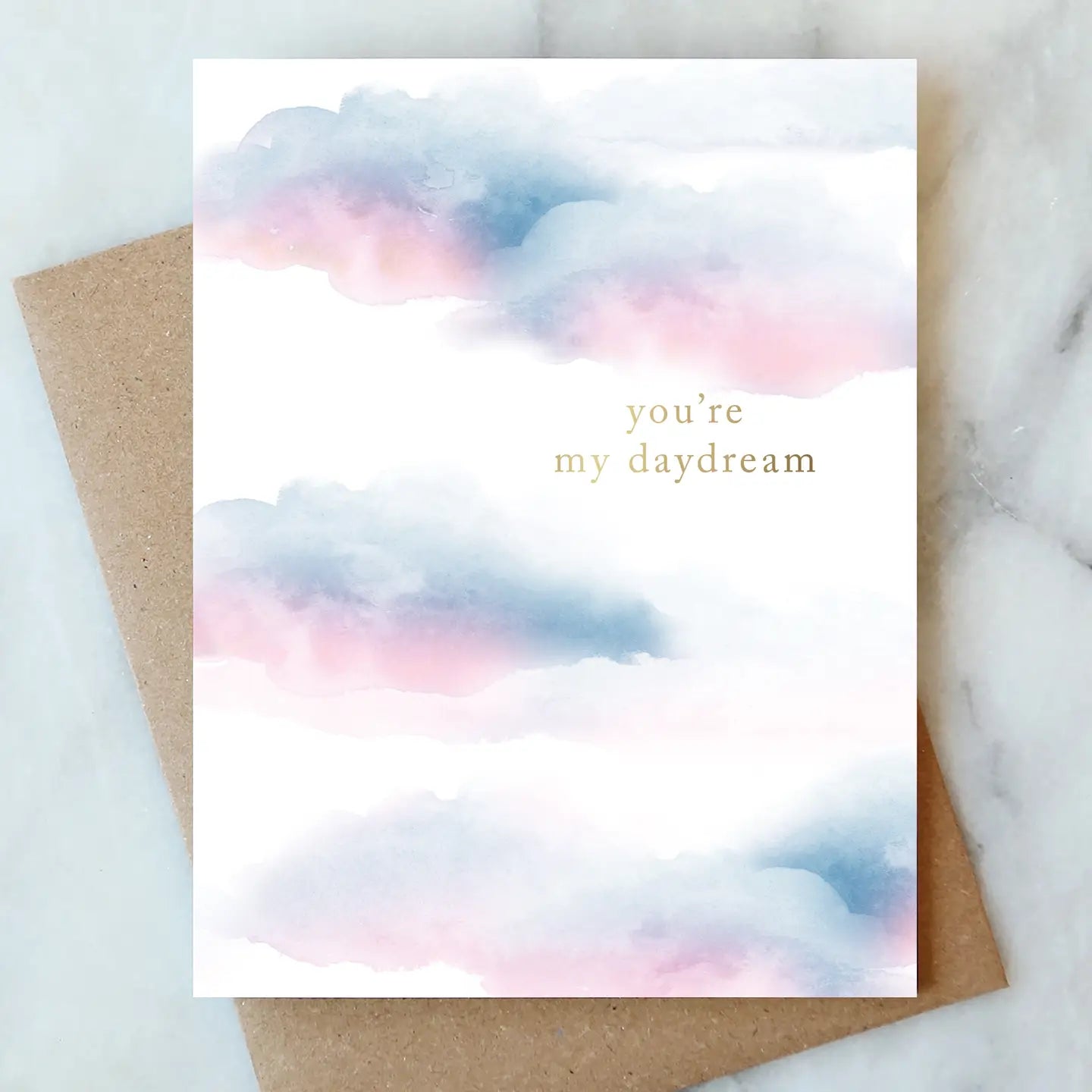 Greeting card with watercolor clouds and text 'you're my daydream' on a marble surface.