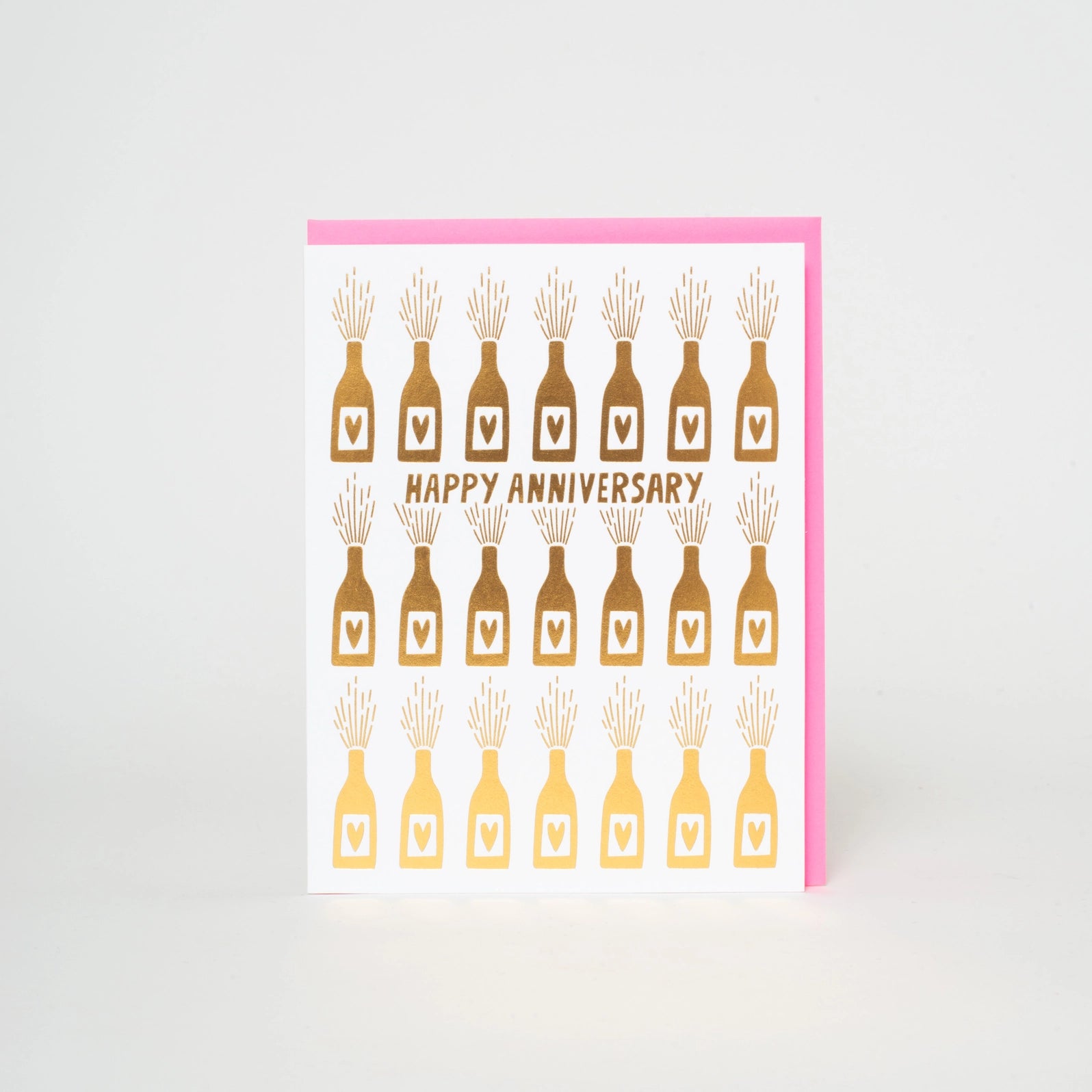 A greeting card with a floral pattern and the text 'HAPPY ANNIVERSARY' in gold foil, accompanied by a fluorescent pink envelope.