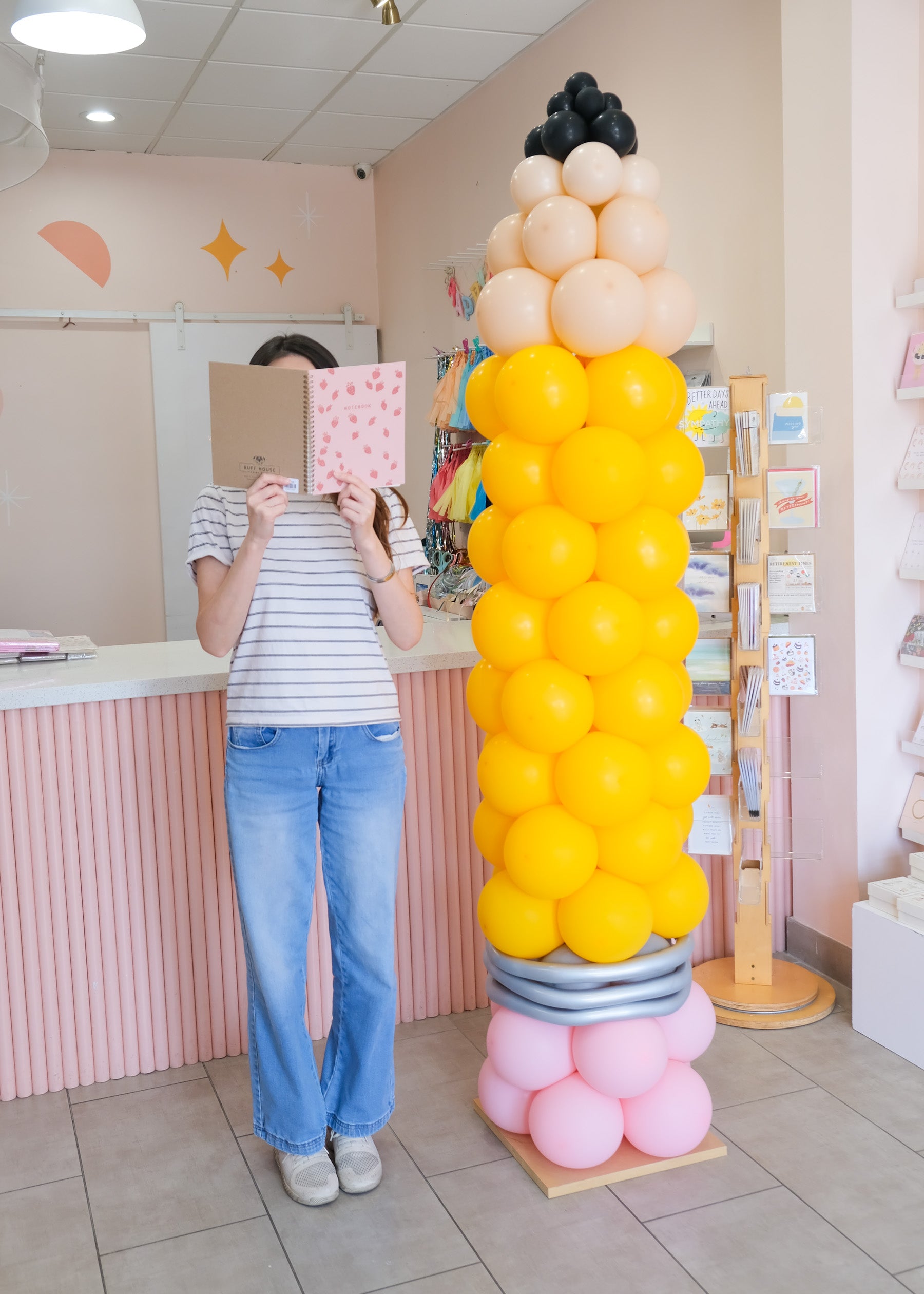 a person reading a notebook next to pencil balloon column for scale
