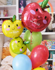 A set of colorful balloons designed to look like apples with the name 'Luca' and the grade '1st Grade' printed on them, along with a handmade tassel.
