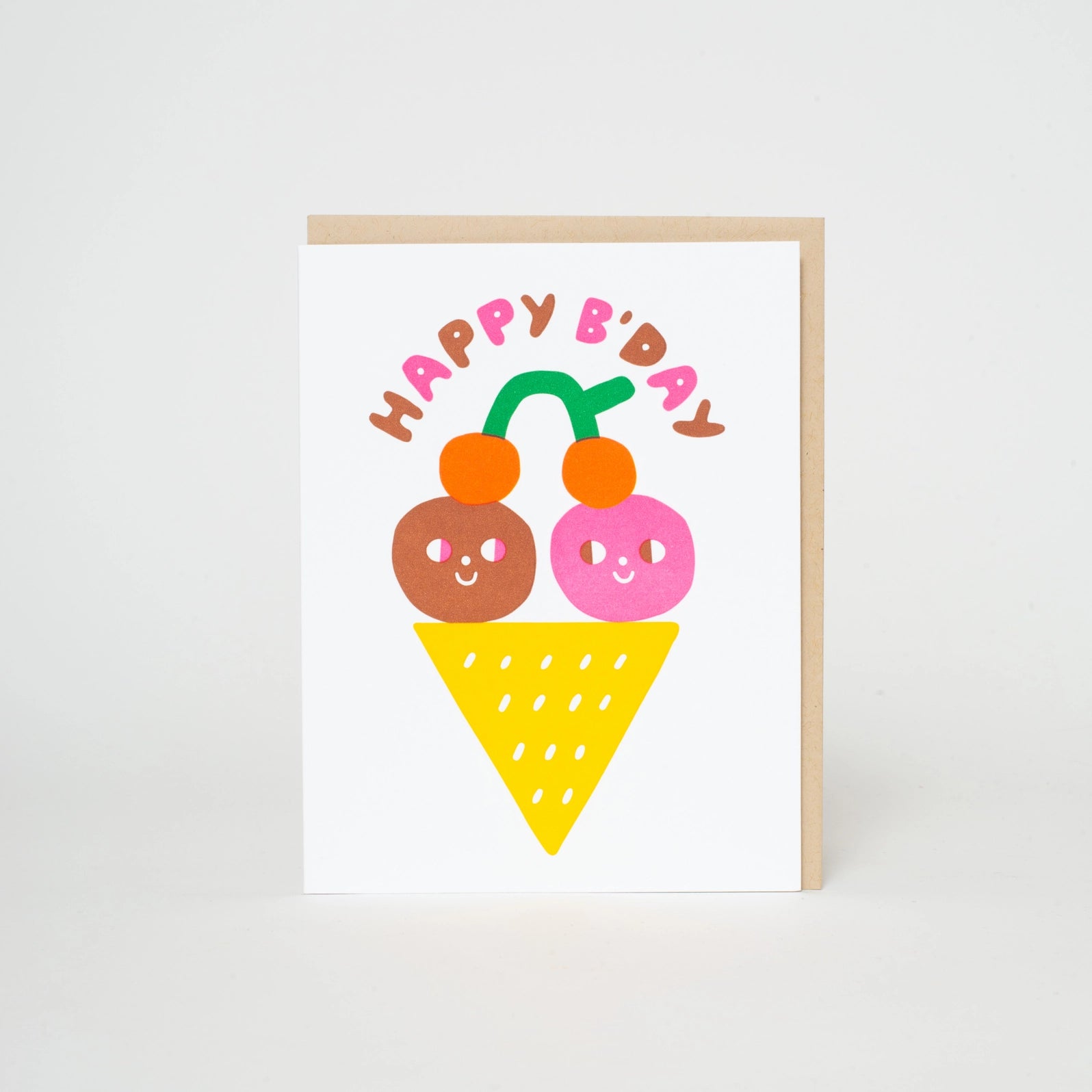 A greeting card with an illustration of two cartoon-style ice cream scoops with faces and a 'Happy B'day' text above. The card is white with a kraft envelope behind it.