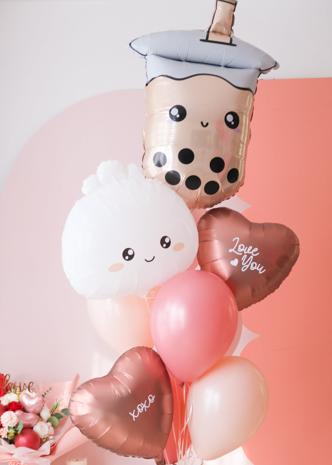 A balloon bouquet featuring a boba bubble tea character balloon, a dumpling with a heart face balloon, and a variety of other balloons in pink, red, and white colors with 'love you' and 'xoxo' decals.