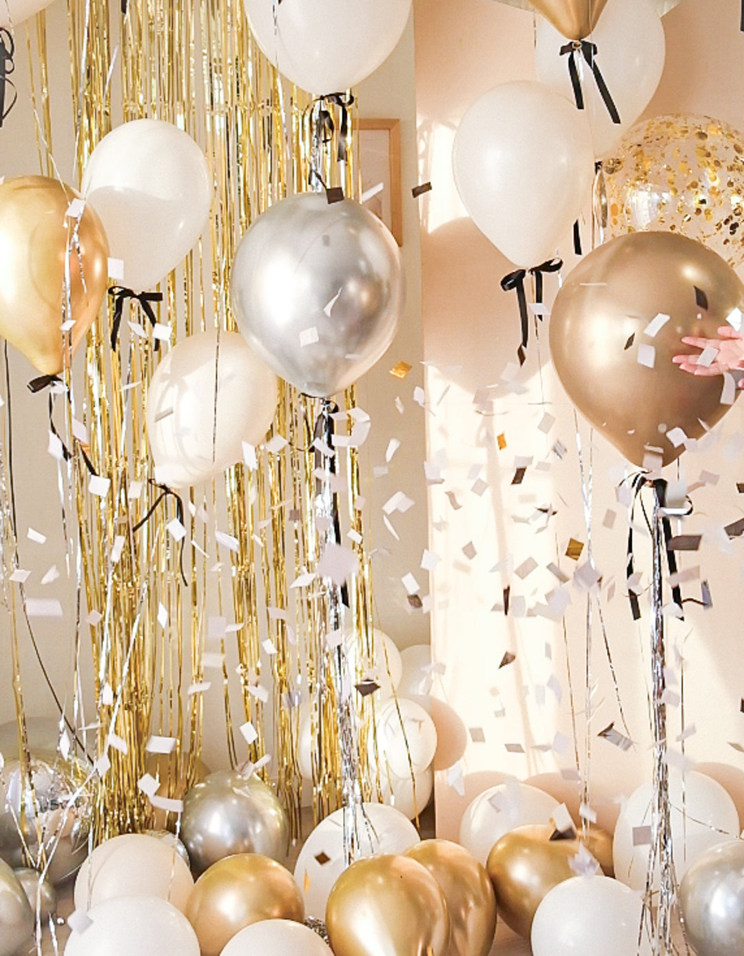 Cream round balloon popped with confetti floating around. Floating balloon with black ribbon bows surrounding.